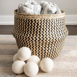 Set of 6 large, premium wool dryer balls next to Mexican Palm woven basket in black and natural with laundry inside