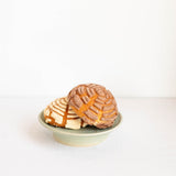 Two Mexican concha pastries on a small light green ceramic cake stand against a clean white background.