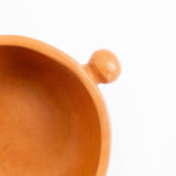 Close-up of a terracotta ceramic bowl with a round side knob, shown against a plain white background. Burnished ceramics from Nahuatl community in Michoacan, Mexico.