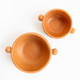 Two terracotta Mexican ceramic bowls with round ball side handles on a white background. Burnished ceramics from Nahuatl community in Michoacan, Mexico.