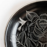 Close-up of a black Huancito ceramic plate with white hand-painted floral and bird motifs common in Michoacan.