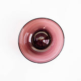 A top-down view of an amethyst glass bowl with a dark rim, set against a plain white background.
