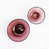 Two round handblown amethyst glass bowls photographed from above on a plain white background.