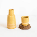 A small yellow ceramic vase/bedside water carafe and matching lid on a wooden base, photographed on a clean white background.
