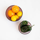 Two amethyst glass bowls on a white background, one containing oranges and lemons and the other containing green jalapeños.