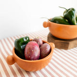 A terracotta Mexican ceramic bowl with ball side handles, filled with green peppers and tuna fruit. Burnished ceramics from Nahuatl community in Michoacan, Mexico.
