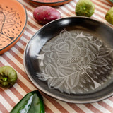 Huancito Mexican burnished ceramic hand-painted plates with floral designs, styled on a striped tablecloth with fresh vegetables.