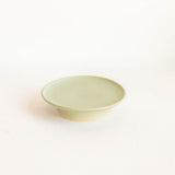 A small round ceramic cake stand dish with a pale sage green glaze, photographed on a clean white background.
