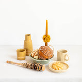 A styled tabletop arrangement featuring Oaxacan beeswax taper candle, Mexican sweet bread, Mexican ceramic mugs and a traditional molinillo whisk. 