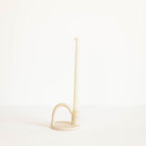 A minimalist cream-colored ceramic candle holder with a single taper candle, set against a seamless white background.