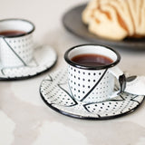 White expresso set of 2 enamel cups and saucers with geometric designs on a marble countertop