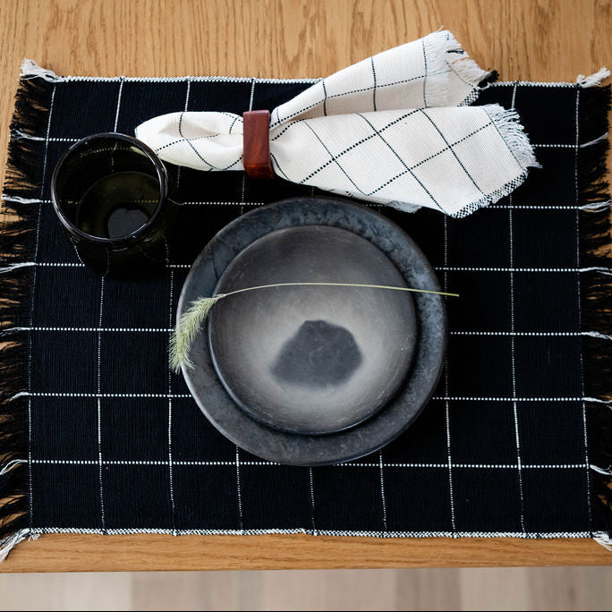 Black and white checkered placemat with a bowl and cups on a wooden table