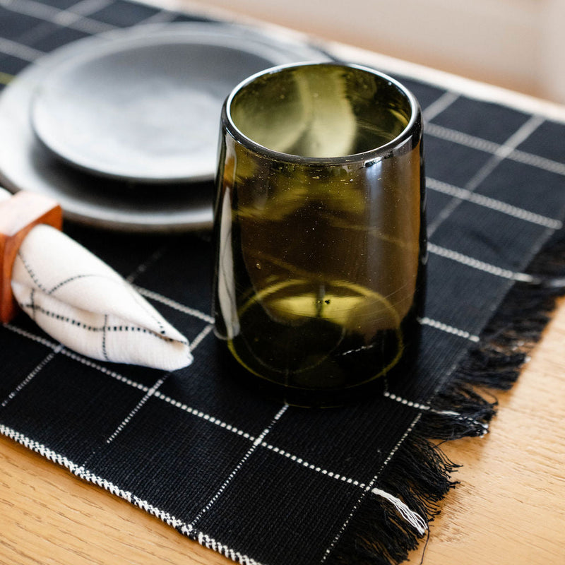 Green glass mug on a black cotton checkered placemat with a neutral background