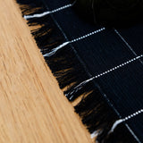 Close-up of a black and white checkered cotton placemat with frayed edges on a wooden dinner table.