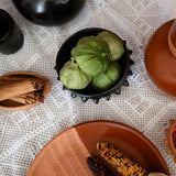 Spices and herbs on a textured surface with a focus on a black ceramic serving bowl.