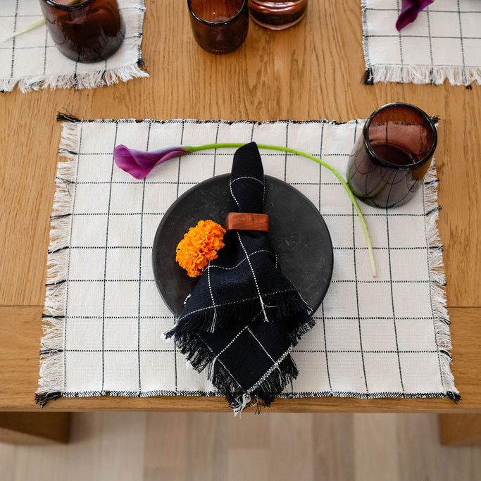 Table setting with black plate, floral arrangement, and glasses on a checkered placemat.