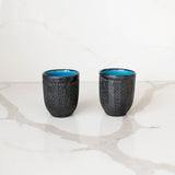 Two black  Modern Mexican ceramic cups with blue interior on a white marble surface