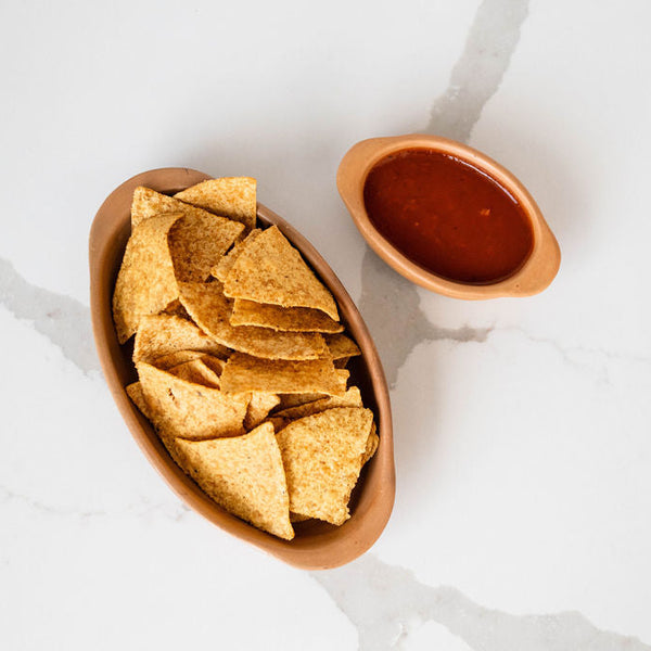 Terracotta Ceramic Clay Bowl of tortilla chips with a small container of salsa on a marble surface