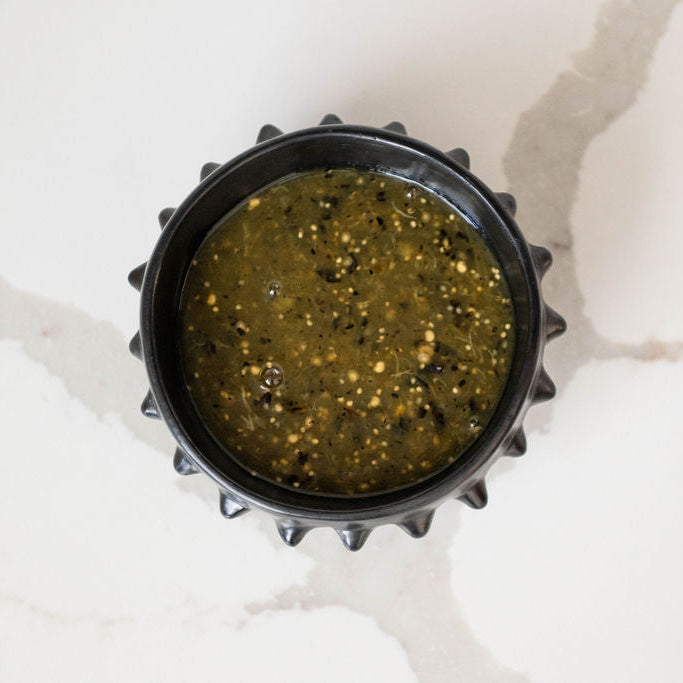 Black Ceramic (Barro Negro) bowl with pointed detail on the rim and salsa verde inside on a marbled background