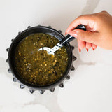 Hand stirring a salsa verde inside a black ceramic serving bowl on a white background