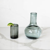 Grey /smoke-colored glass carafe with lid that serves as cup on marble countertop