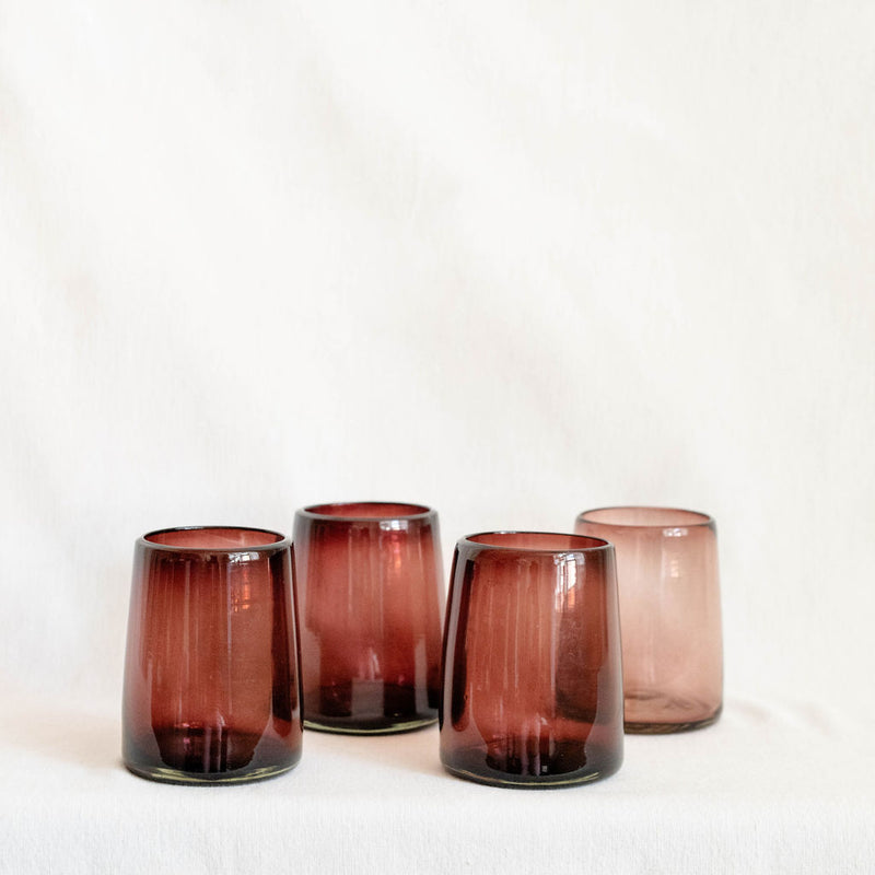 Four purple pink glass tumblers on a white background
