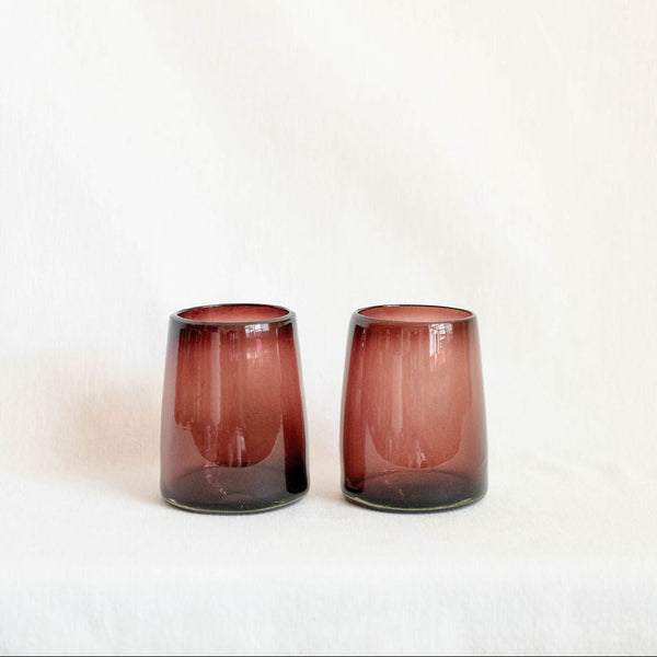 Two purple pink glass tumblers on a white background