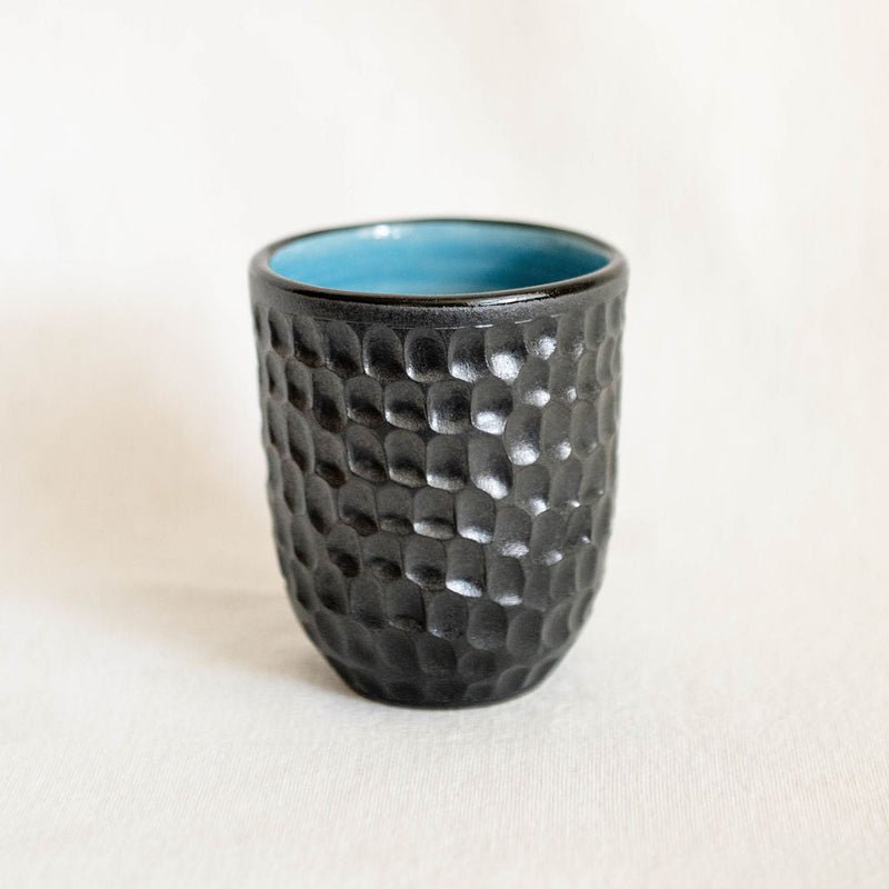 Black textured ceramic cup with a blue interior on a white background