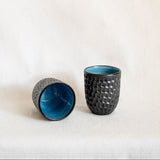 Two textured ceramic cups with blue interior on a white background