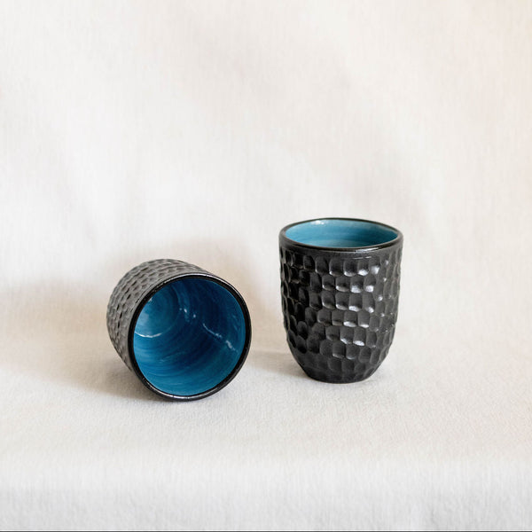 Two textured ceramic cups with blue interior on a white background