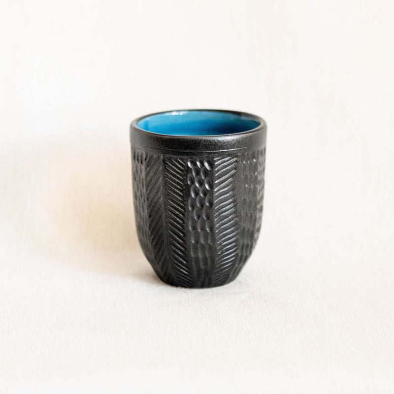 Black textured ceramic cup with a blue interior on a white background