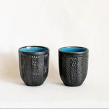 Two black textured ceramic cups with blue interior on a white background