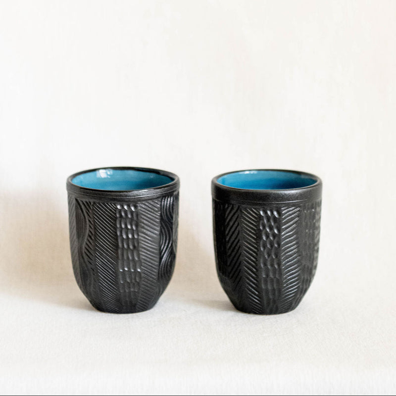 Two black textured ceramic cups with blue interior on a white background