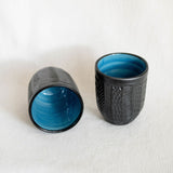 Two textured black ceramic cups with blue interior on a white background