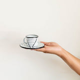 Hand holding an enamelware espresso cup and saucer