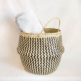 Woven basket with zigzag pattern containing a white towel on a light background