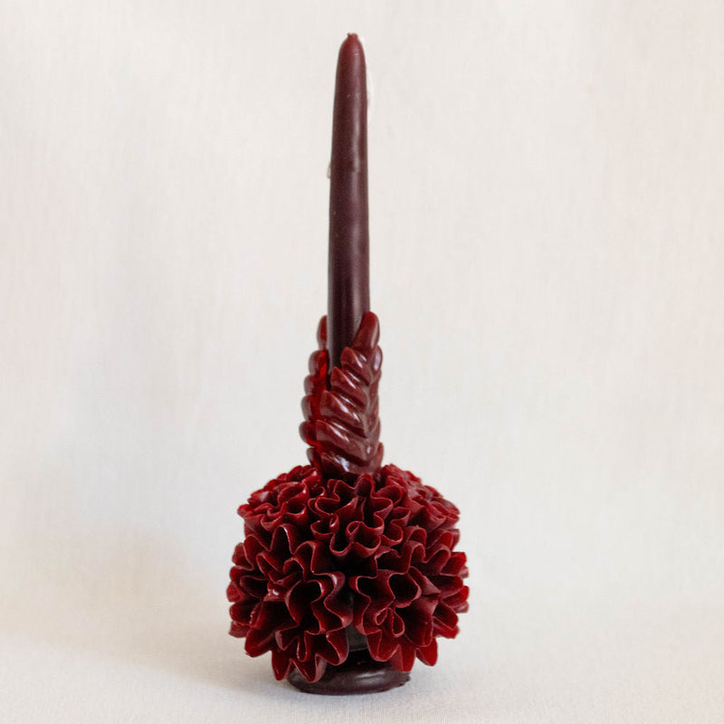 A handcrafted Oaxacan beeswax candle in a red burgundy featuring intricate floral designs that showcase traditional artistry. 