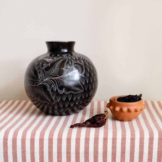 Black decorative vase with intricate patterns on a striped tablecloth.