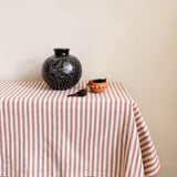 Table with a cinnamon and white striped tablecloth, black vase, and small bowl against a beige wall.