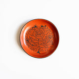 Red orange burnished ceramic plate from Huancito with black floral design on a white background