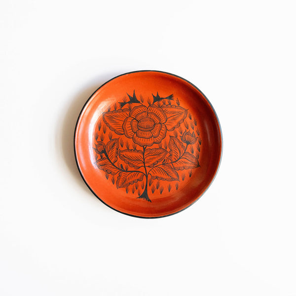 Red orange burnished ceramic plate from Huancito with black floral design on a white background