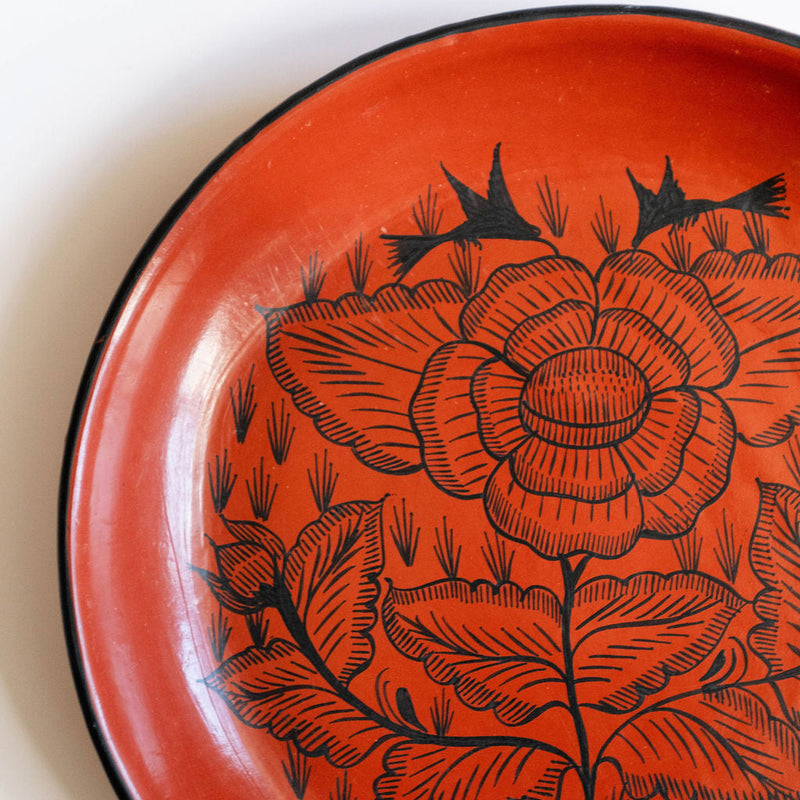 Closeup of a red orange burnished ceramic plate from Huancito with black floral design on a white background