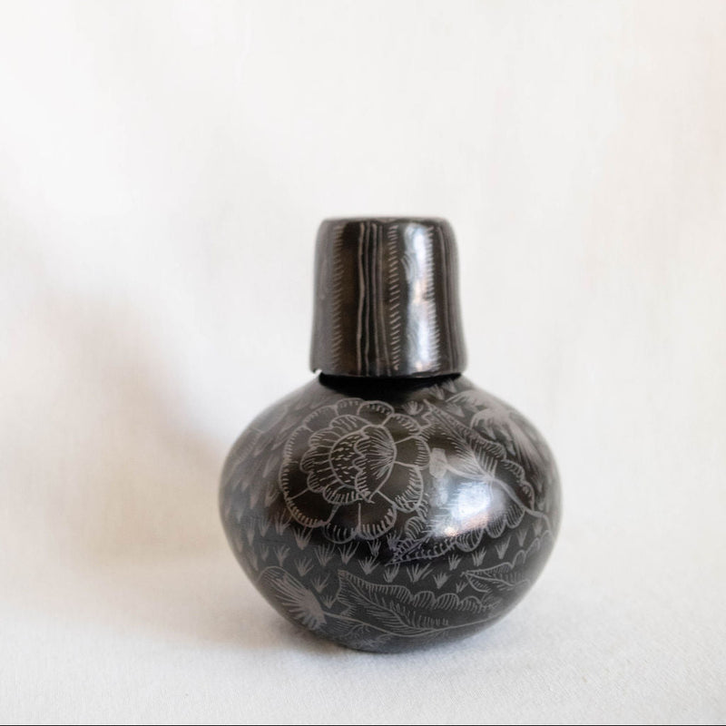 Decorative black carafe with intricate patterns on a white background