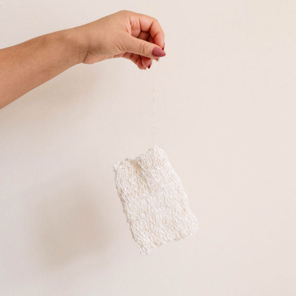Hand holding an agave fiber soap bag with drawstring against a plain background