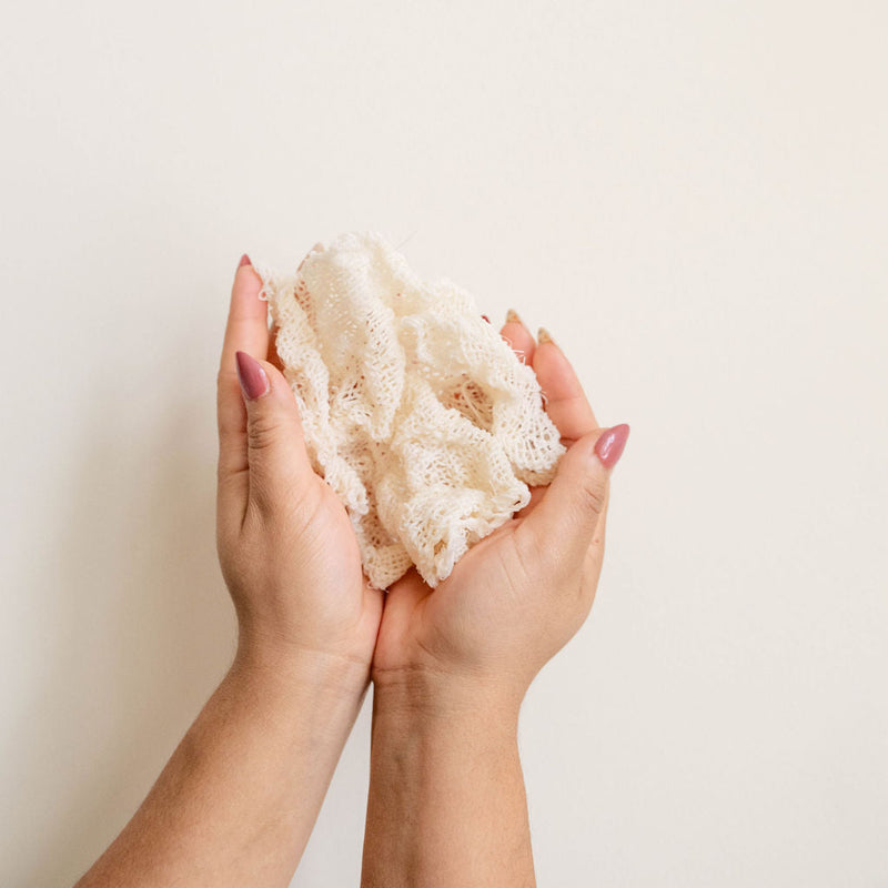 Hands holding an agave ayate washcloth against a plain background