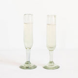 Two clear glass champagne flutes with stems and circular bases, standing upright on a seamless white background.