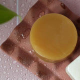 Coconut and almond dip conditioner bar resting on a surface. The creamy, round bar is rich in natural oils and designed for eco-friendly, zero-waste hair care.