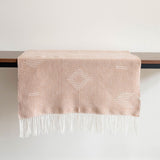 Mahogany brown cotton woven table runner with geometric designs and white fringe on table with a white background