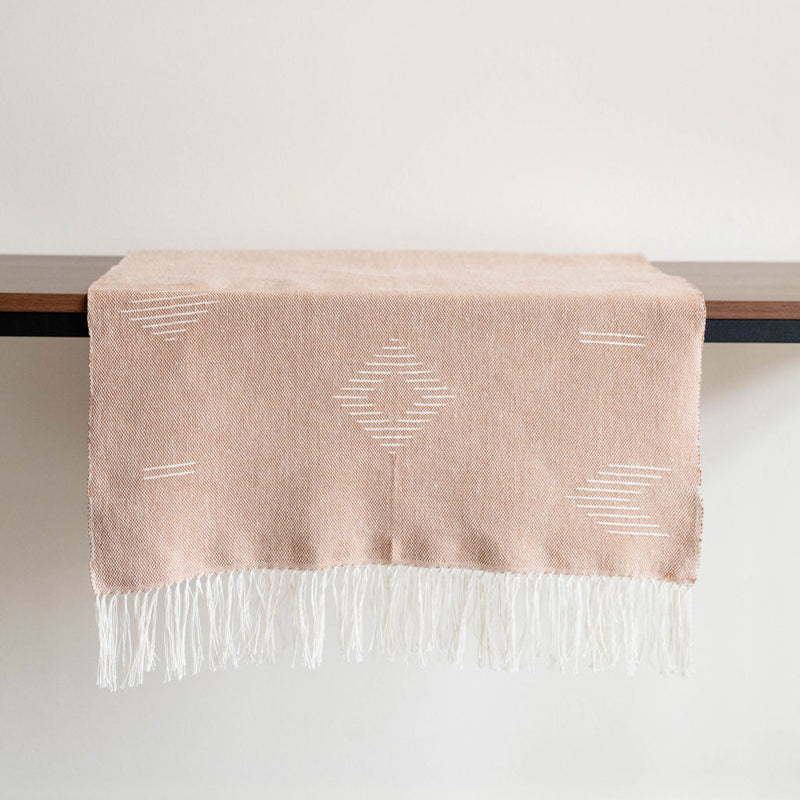 Mahogany brown cotton woven table runner with geometric designs and white fringe on table with a white background