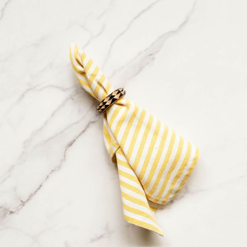Yellow and white striped cloth dinner napkin with wood napkin ring on a marble surface